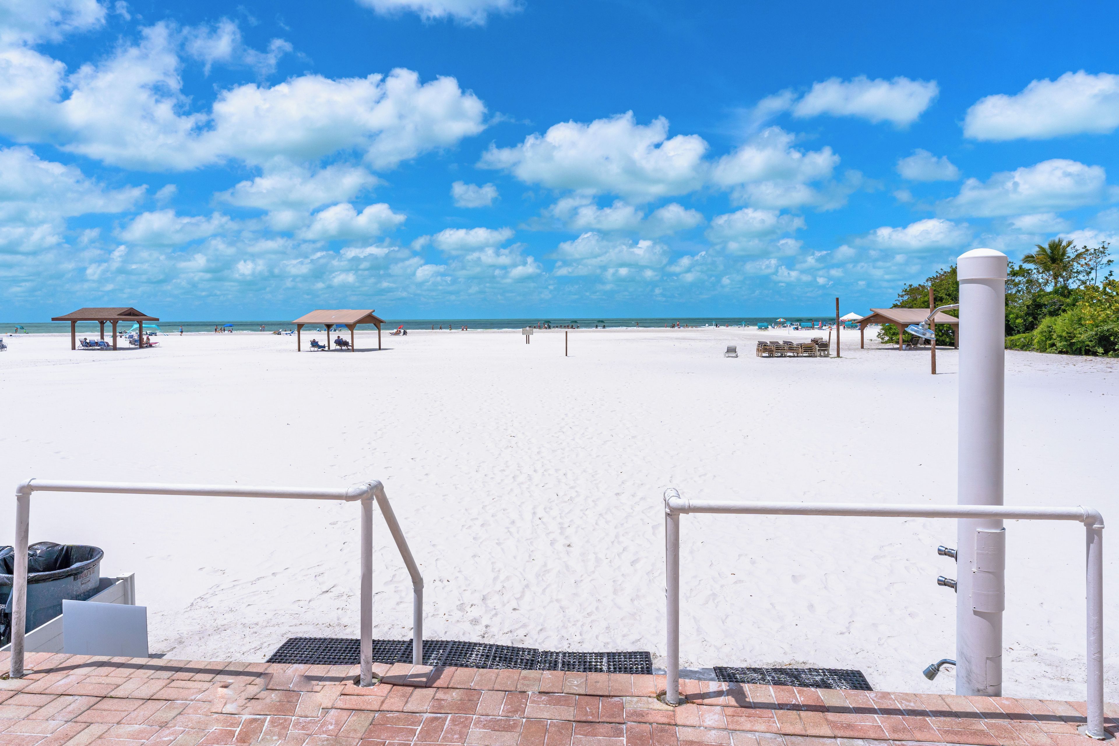 A beach with a clear sky, a sandy shore, and a few beach huts.