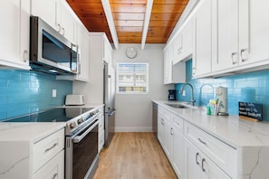 A modern kitchen with white cabinets, a stainless steel oven, a microwave, and a wooden ceiling. - Casa Mar By Beachside Management (Siesta Key)