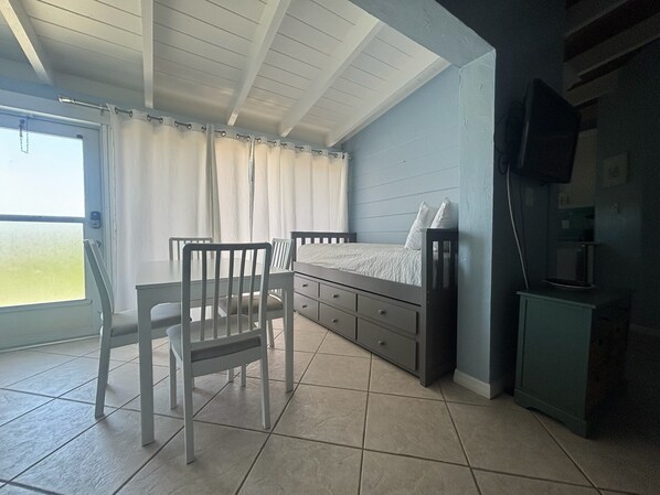 A bedroom with a bed, a chair, a dresser, a television, and a window with curtains. - Casa Mar By Beachside Management (Siesta Key)