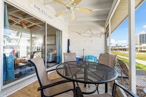 A covered outdoor area with a round metal table and chairs, a ceiling fan, and a view of the surrounding area. - Casa Mar By Beachside Management (Siesta Key)