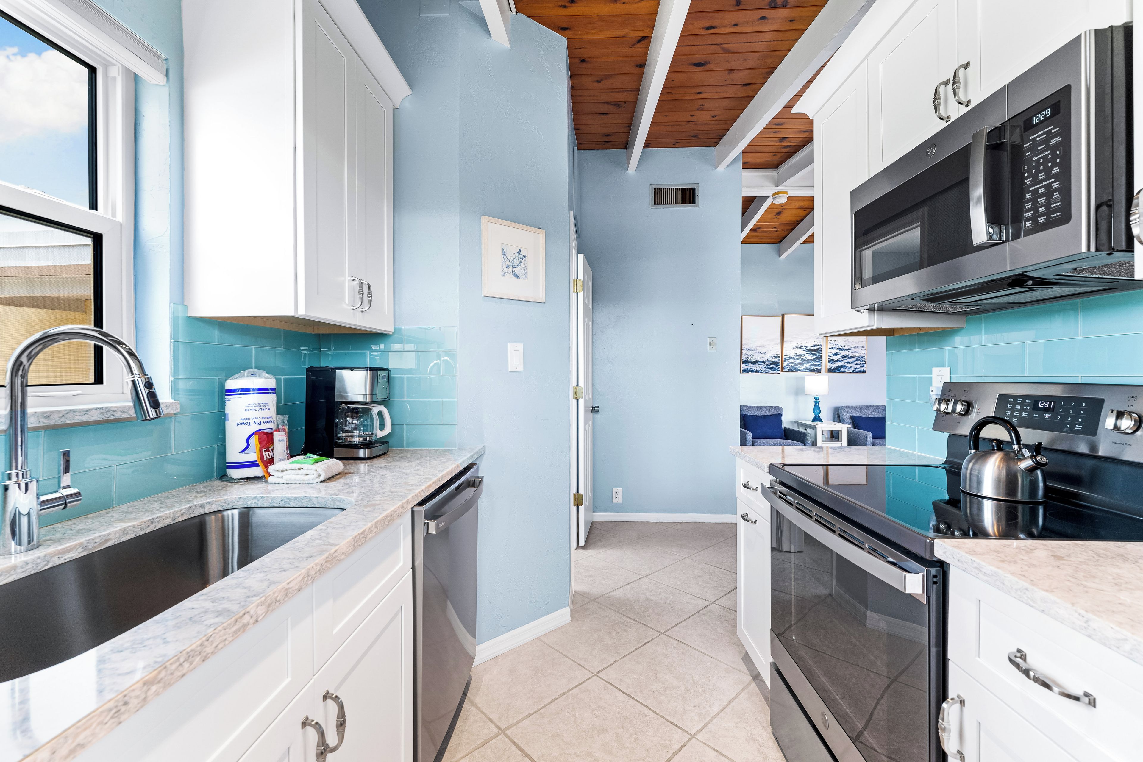 A modern kitchen with white cabinets, a stainless steel sink, a coffee maker, and a kettle.