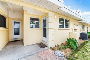 A two-story residential building with a yellow exterior, numbered doors, and a small front porch with a doormat.