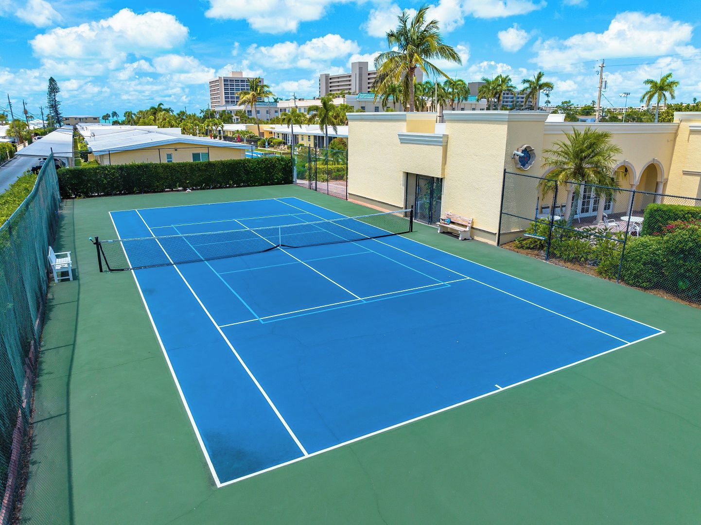Una cancha de tenis con red, rodeada por una valla, y una banca.