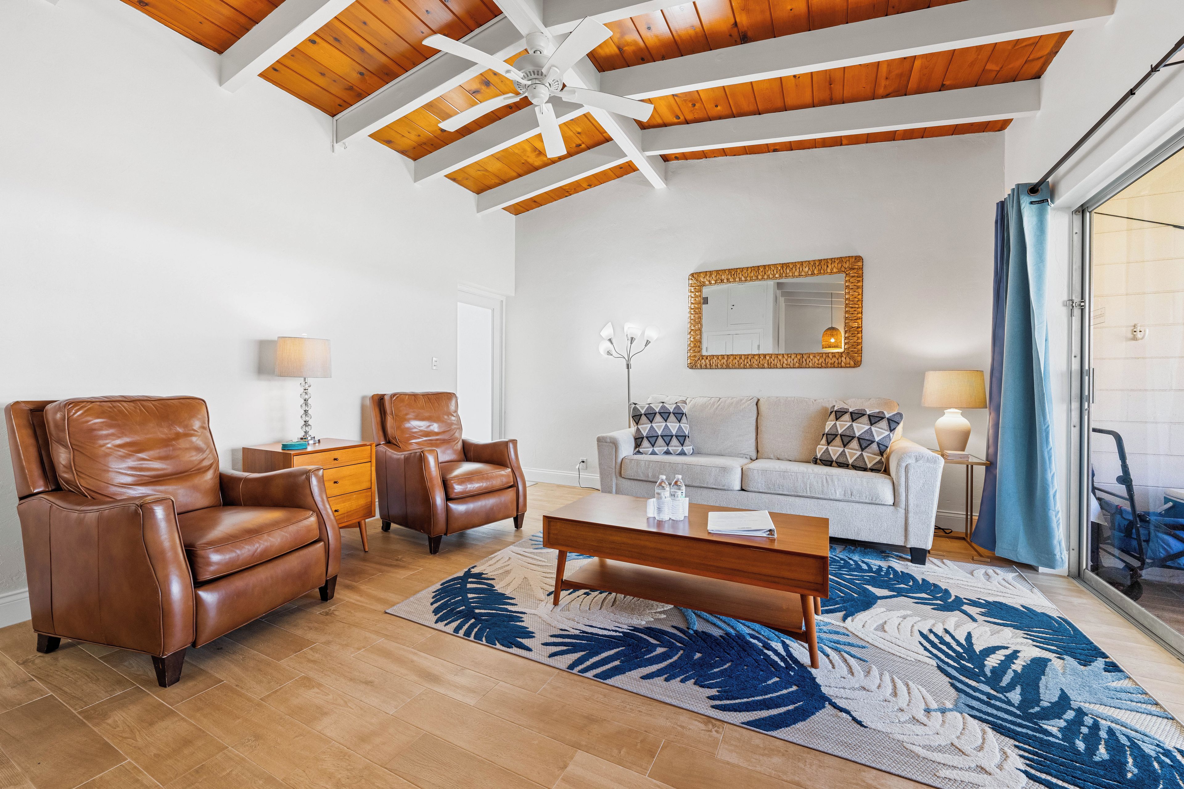 A living room with a wooden ceiling, a sofa, two leather chairs, a coffee table, and a large patterned rug.
