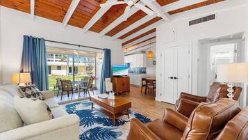 Uma sala de estar ampla com teto de madeira, uma janela grande com cortinas, um sofá, uma mesa de centro e vista para o exterior.
