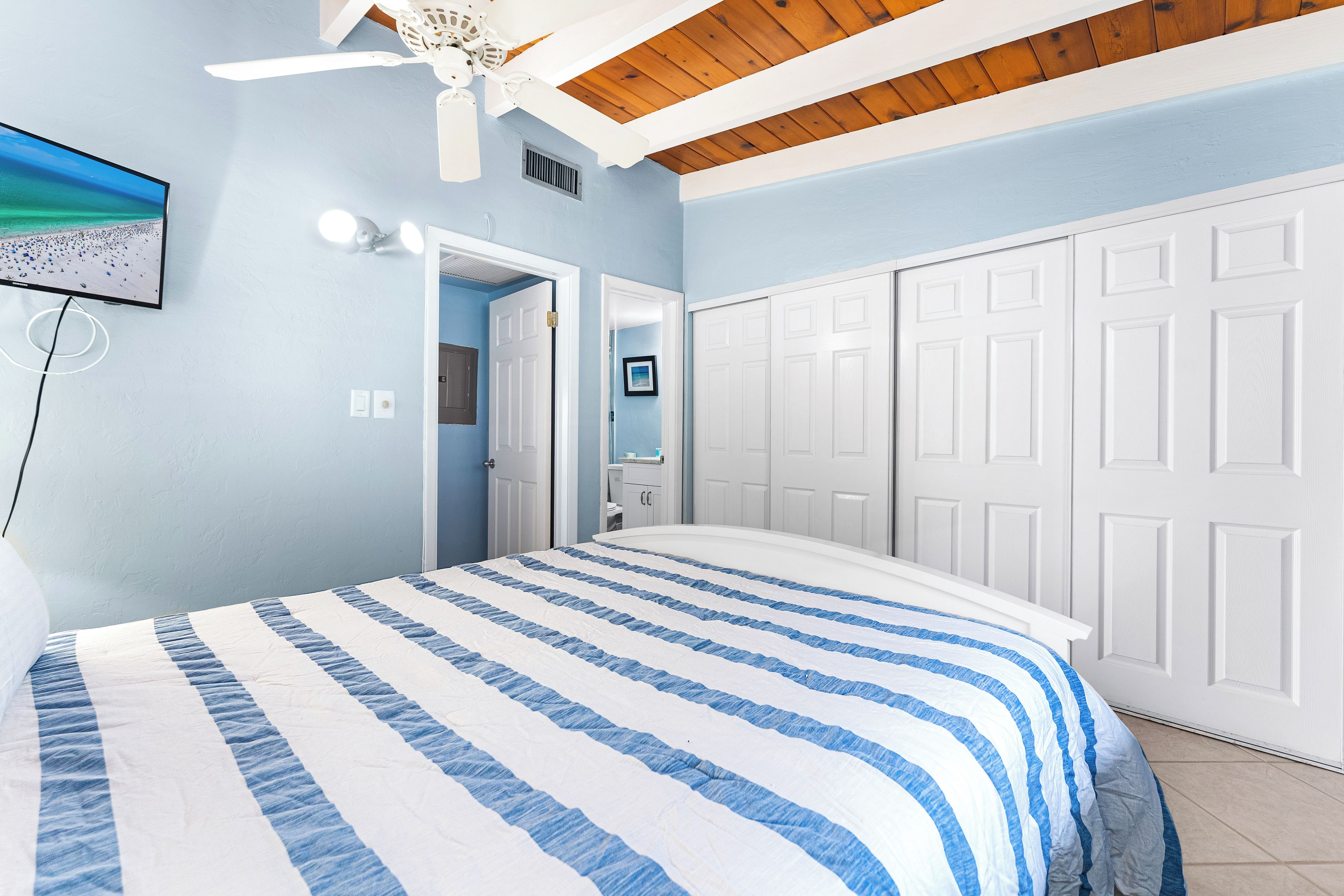 A bedroom with a bed, a ceiling fan, a TV, and a wardrobe.