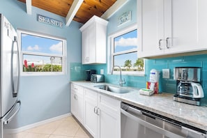 Una cocina con armarios blancos, un refrigerador de acero inoxidable, una cafetera y vista al mar.