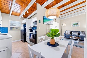 A modern kitchen with white cabinets, a dining area with a white table, and a living room with a blue sofa. - Casa Mar By Beachside Management (Siesta Key)