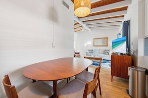 A dining area with a wooden table and chairs, a hanging light fixture, a television, and a trash can. - Casa Mar By Beachside Management (Siesta Key)