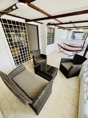 A covered patio area with wicker furniture, a glass-top table, and a hammock. - Hotel Tamaca House (Santa Marta)