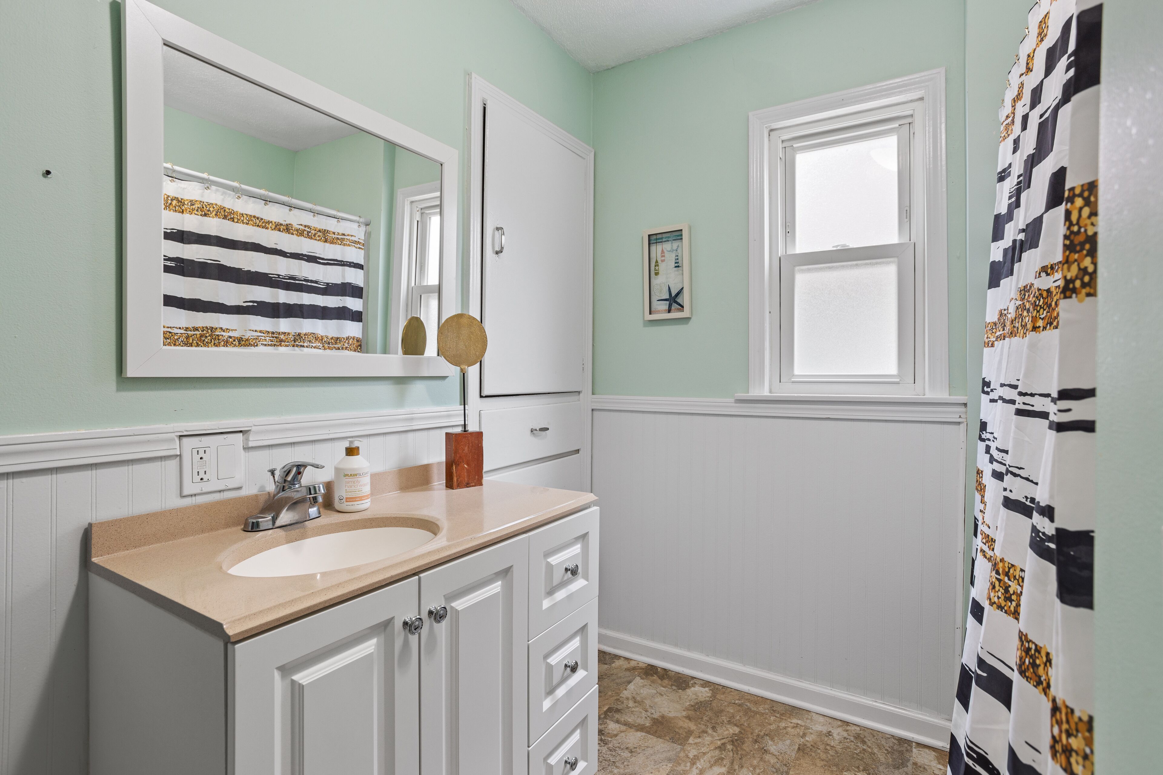 A bathroom with a sink, mirror, and window.