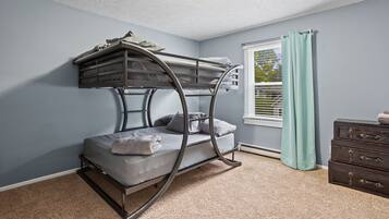 A bunk bed in a room with light blue walls, a window with blinds, and a dresser.