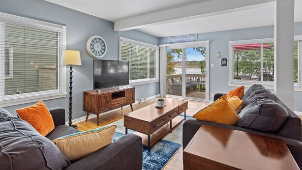 A living room with a TV, wooden furniture, and a sign reading "BEACH HOUSE". - Park Lake Getaway (East Lansing)