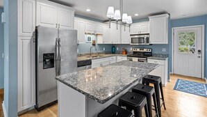 A modern kitchen with white cabinets, stainless steel appliances, granite countertops, and bar stools. - Park Lake Getaway (East Lansing)