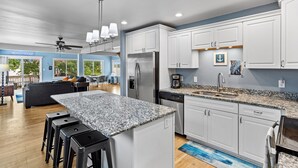 A modern kitchen with white cabinets, granite countertops, and stainless steel appliances. There is a bar area with stools and a dining table in the background. - Park Lake Getaway (East Lansing)