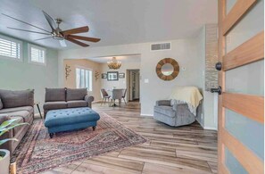 Relax in this stylish living room with a plush ottoman, sofa, and armchair, surrounded by a large window and a chandelier.