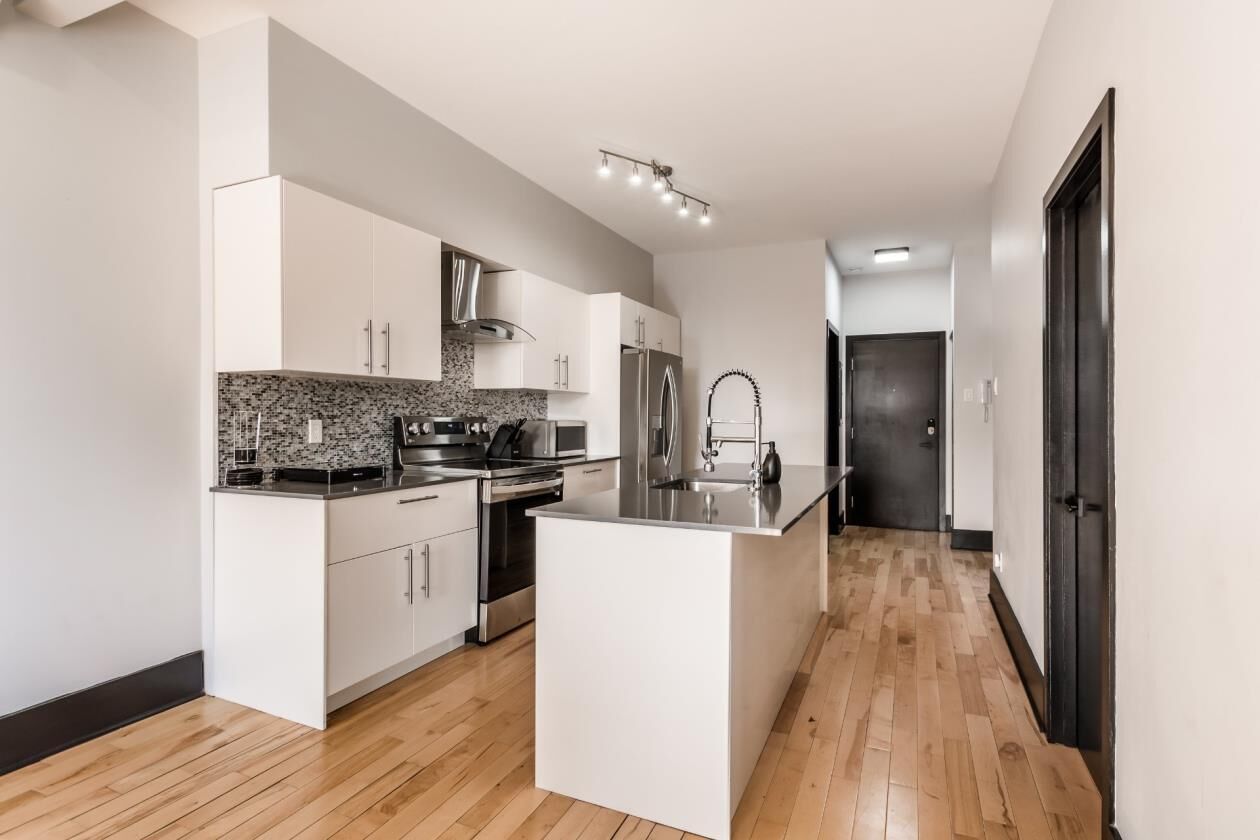 A modern kitchen with white cabinetry, a granite countertop, stainless steel appliances, and a central island.