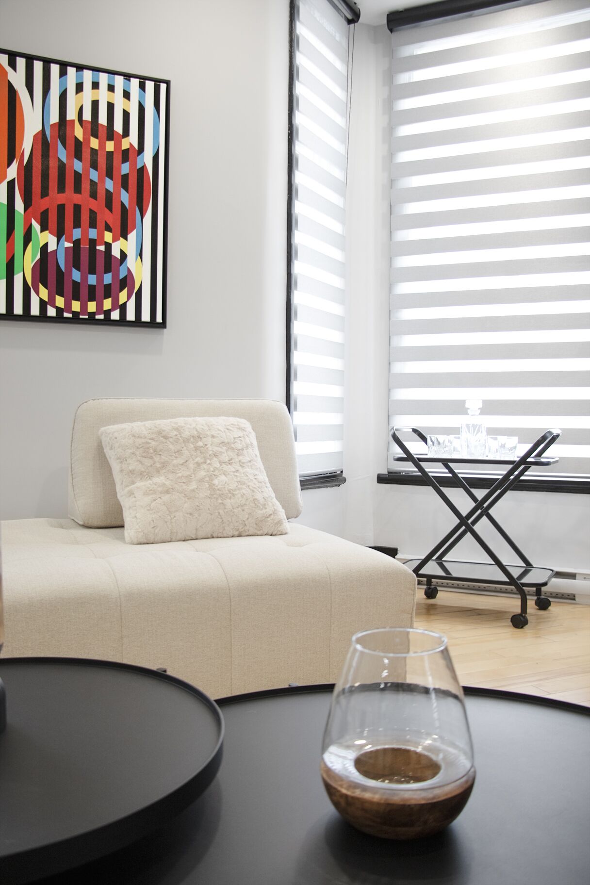 Uma sala de estar moderna com um sofá, uma mesa de vidro com uma taça de vinho e uma pintura abstrata colorida na parede.