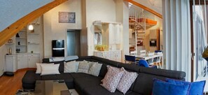 A modern loft-style living space with a black sectional sofa, white cabinets, and a staircase leading to an upper level.