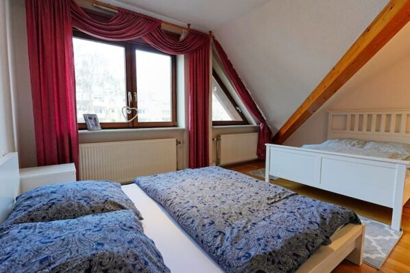 A bedroom with two beds, a window with red curtains, and a sloped ceiling.