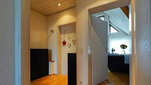 Un pasillo con piso de madera, un armario negro y una puerta que da a una habitación con cama y ventana.
