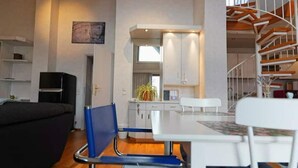 Una sala de estar moderna con un sofá, una mesa de comedor con sillas, una zona de cocina con armarios y una escalera.