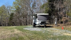 A white RV parked in a grassy area with trees in the background. - Secluded RV Camper Spot (Thomasville)