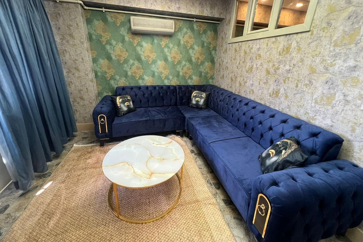 A room with a blue sectional sofa, a round marble coffee table, and patterned wallpaper.