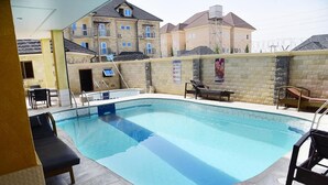 An indoor swimming pool with lounge chairs and a view of residential buildings in the background. - Tokyo Apartments  (Abuja)