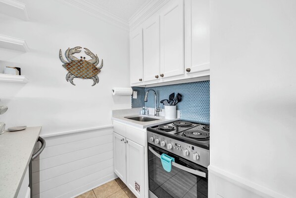 A kitchen with white cabinets, a blue tiled backsplash, a stainless steel sink, and a stove.