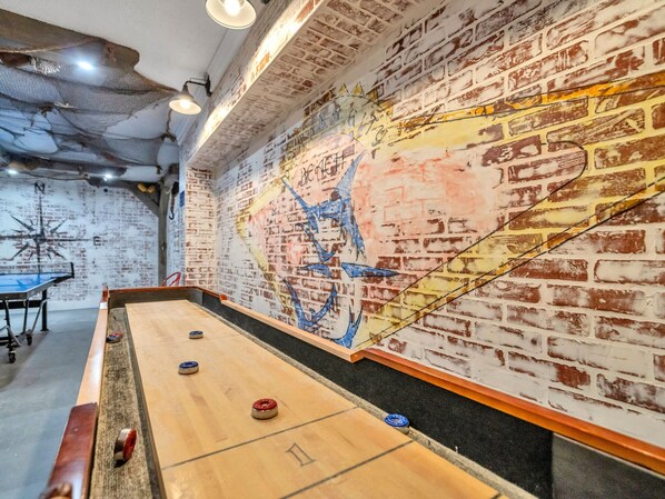 Una mesa de shuffleboard con discos, una pared con un mural y un muro de ladrillos.