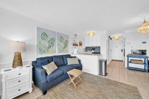 Ein modernes Wohnzimmer mit Sofa, Couchtisch und Lampe. Es gibt eine Küchenzeile mit Schränken und einer Mikrowelle.