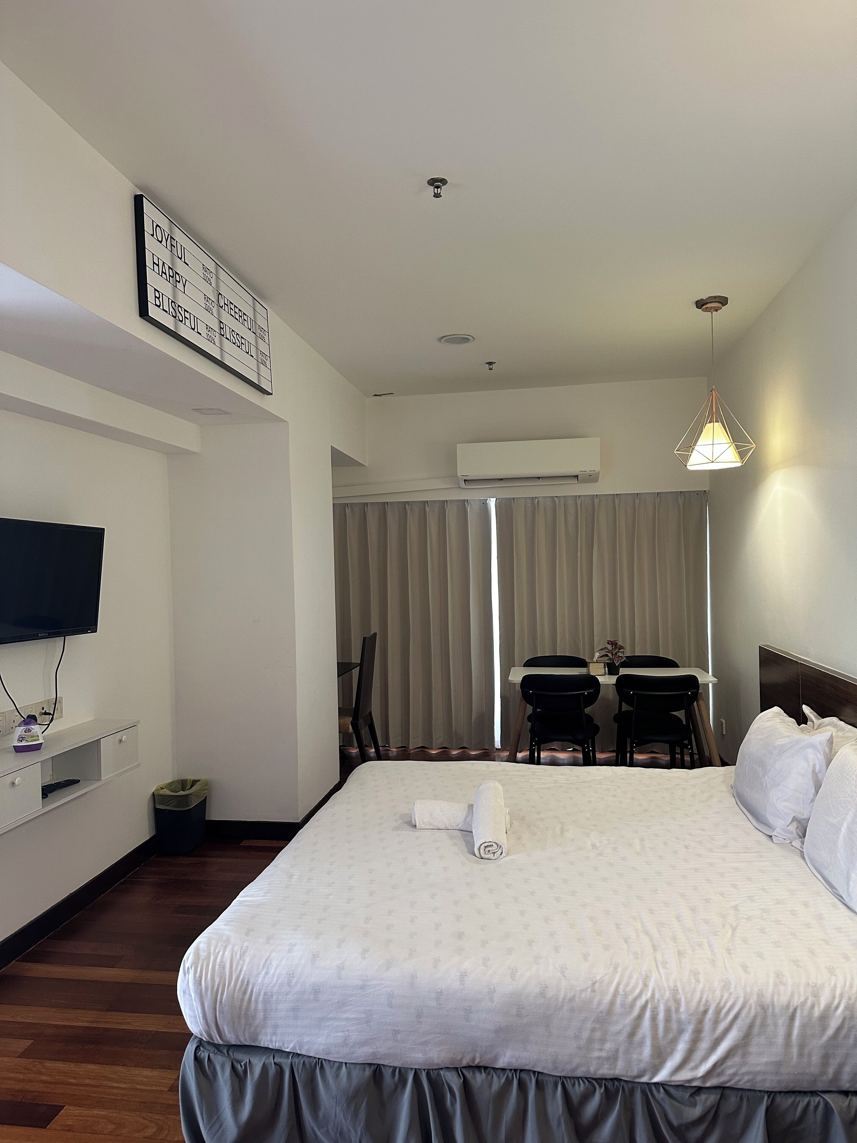 A hotel room with a large bed, a desk with chairs, a television, and an air conditioning unit.