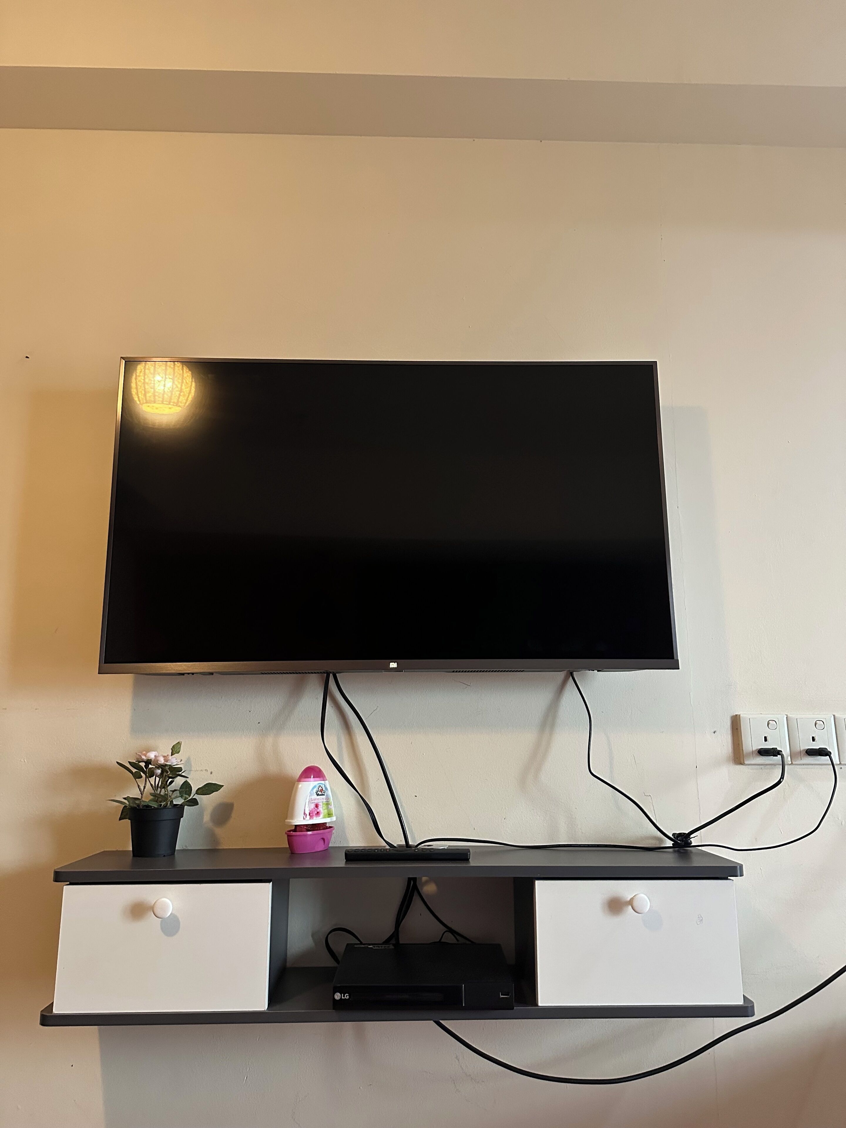 A flat-screen TV mounted on a wall above a black entertainment unit with two drawers.