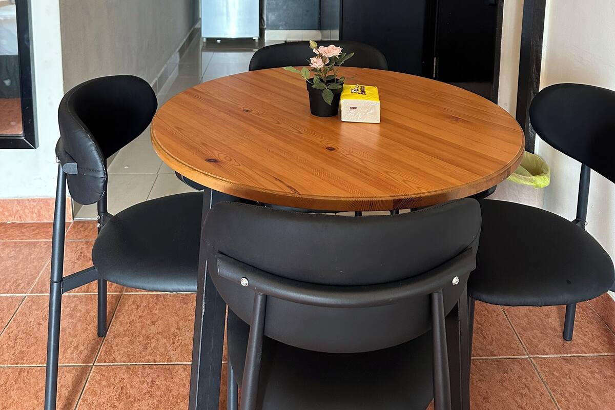 Een compacte keuken met moderne apparaten, een eethoek met een houten tafel en zwarte stoelen, en een kleine potplant.