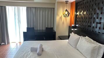 Quarto de hotel com uma cama grande, cabeceira com padrão geométrico, ar condicionado fixado na parede e janela com cortinas.