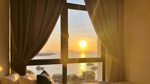 A room with a bed, a window with curtains, and a view of the sunset over water. - Homesuite' Home at The Shore KK (Kota Kinabalu)