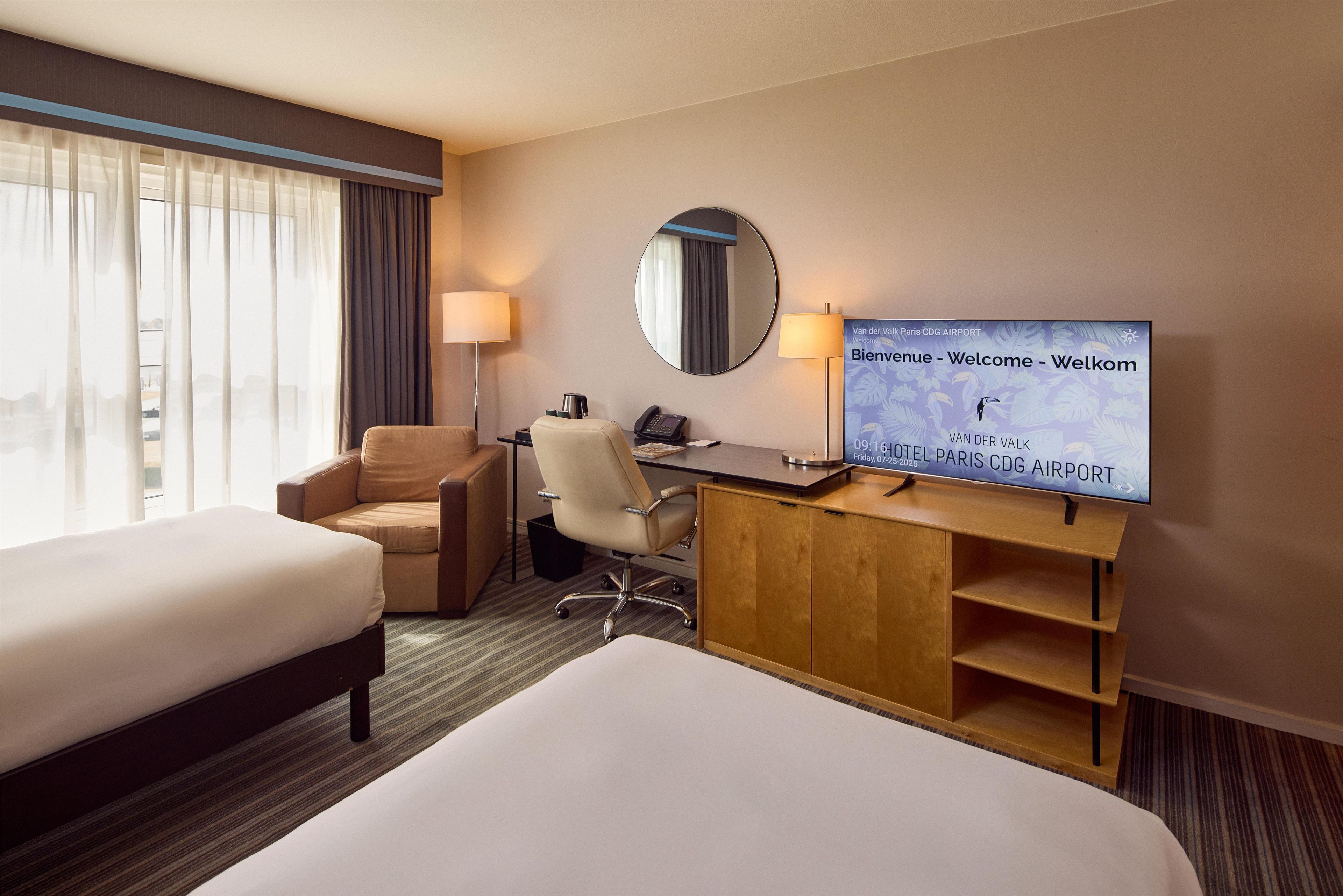 A hotel room with a bed, a desk, a chair, a TV, and a window with curtains.