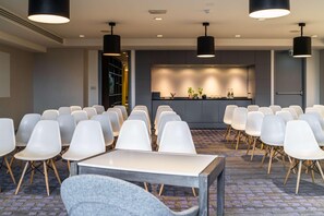 A conference room with rows of white chairs, a long table, and pendant lighting. - Van der Valk Hotel Paris CDG Airport (Roissy-en-France)