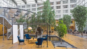 A spacious indoor atrium with a central seating area, surrounded by greenery and a staircase. - Van der Valk Hotel Paris CDG Airport (Roissy-en-France)