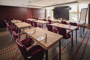 A conference room with multiple tables and chairs, a large screen, and a patterned carpet.