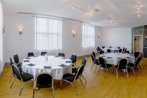 A conference room with multiple round tables, black chairs, and white tablecloths. - Van der Valk Hotel Paris CDG Airport (Roissy-en-France)