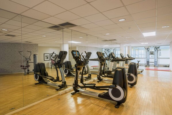 Une salle de sport équipée de nombreux appareils d’exercice, dotée d’un plancher en bois et de grandes fenêtres.