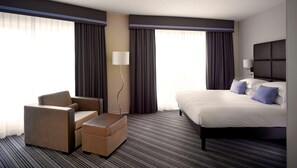 A hotel room with a bed, a chair, a small table, and a lamp. - Van der Valk Hotel Paris CDG Airport (Roissy-en-France)