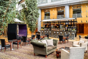 A spacious indoor area with a bar, seating arrangements, and a large tree. - Van der Valk Hotel Paris CDG Airport (Roissy-en-France)