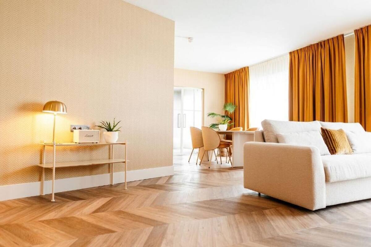 A modern living room with a sofa, a coffee table, and a lamp. There is a dining area with chairs and a table in the background.