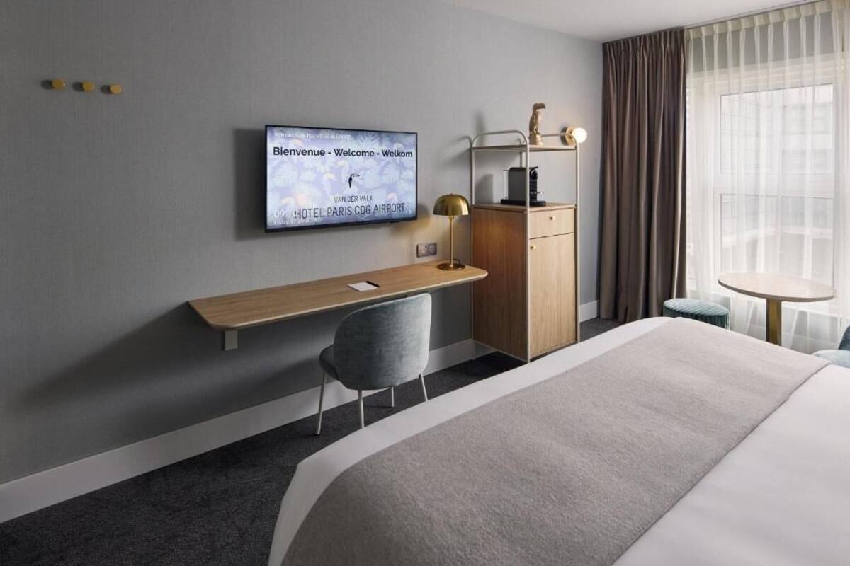 A modern hotel room with a bed, a desk, a chair, a TV, a wardrobe, and a window with curtains.