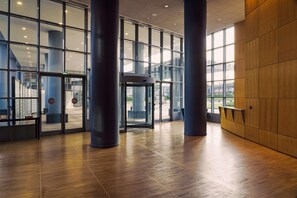 Un hall d’entrée spacieux au design moderne, avec une entrée en verre, de grandes colonnes et un plancher en bois.