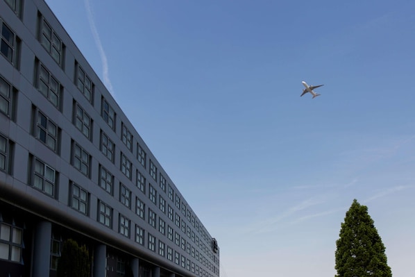 A modern building with a clear sky and a plane in flight. - Van der Valk Hotel Paris CDG Airport (Roissy-en-France)