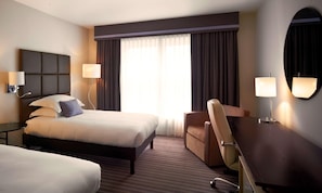 A hotel room with a large bed, a desk, two lamps, a chair, and a large window with curtains. - Van der Valk Hotel Paris CDG Airport (Roissy-en-France)
